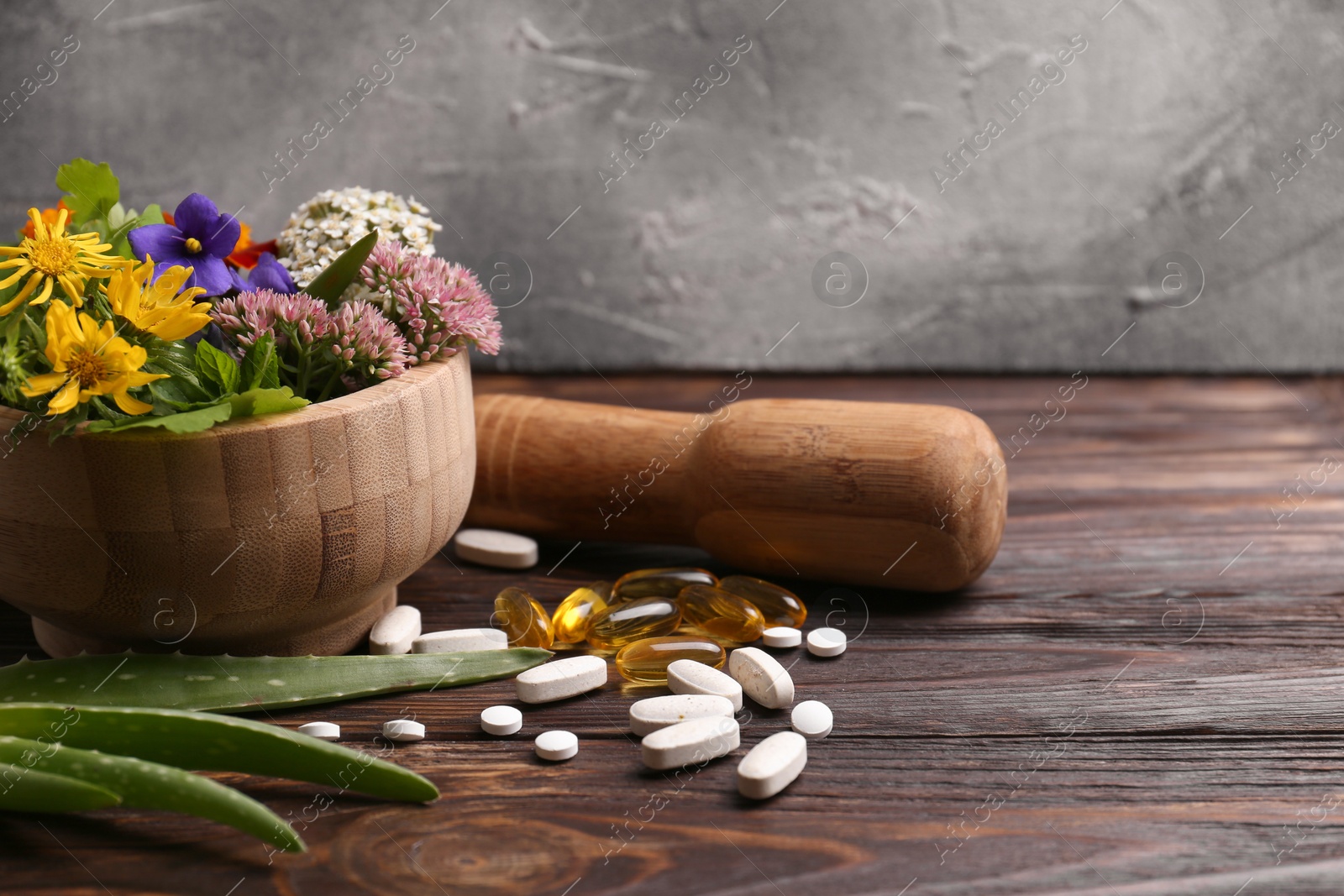 Photo of Mortar with fresh herbs, flowers and pills on wooden table, space for text