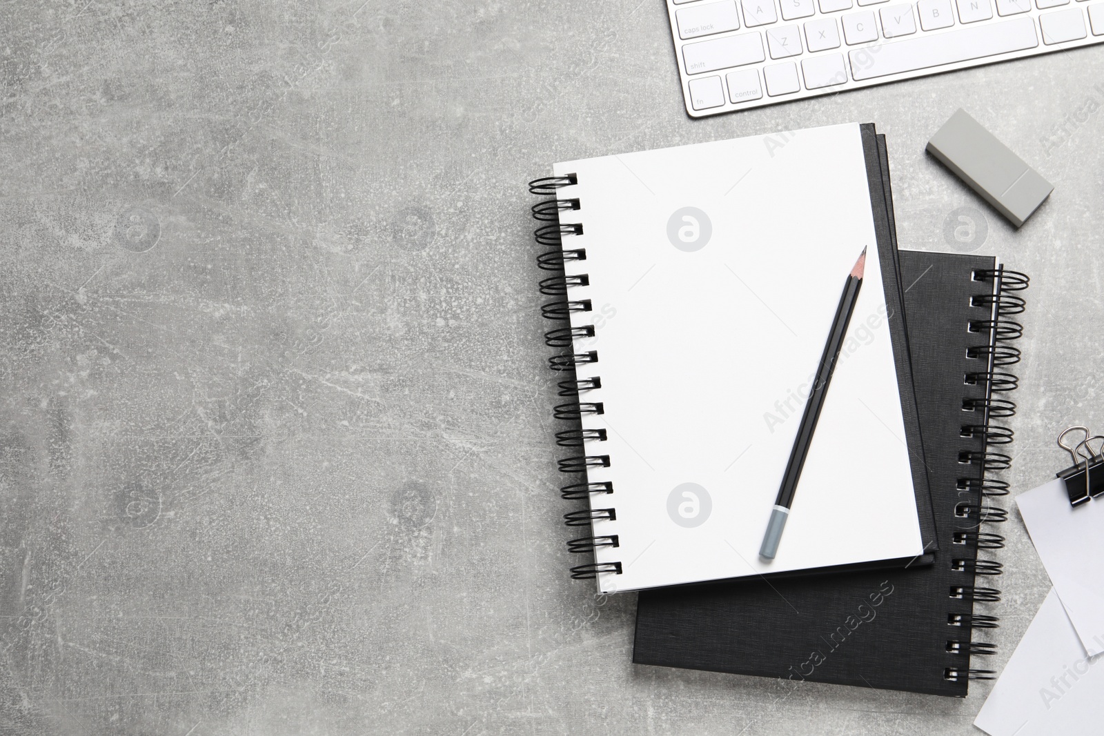 Photo of Open blank notebook, keyboard and stationery on light grey table, flat lay. Space for text