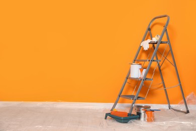 Photo of Ladder, cans of paint and renovation equipment near orange wall indoors. Space for text
