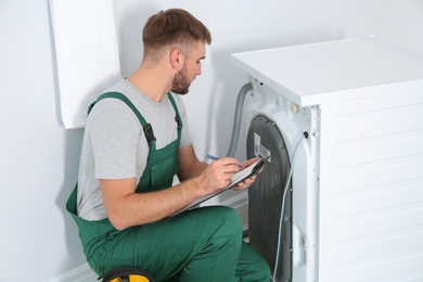 Photo of Young plumber with clipboard examining washing machine in bathroom