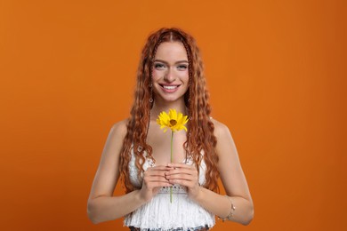 Beautiful young hippie woman with sunflower on orange background