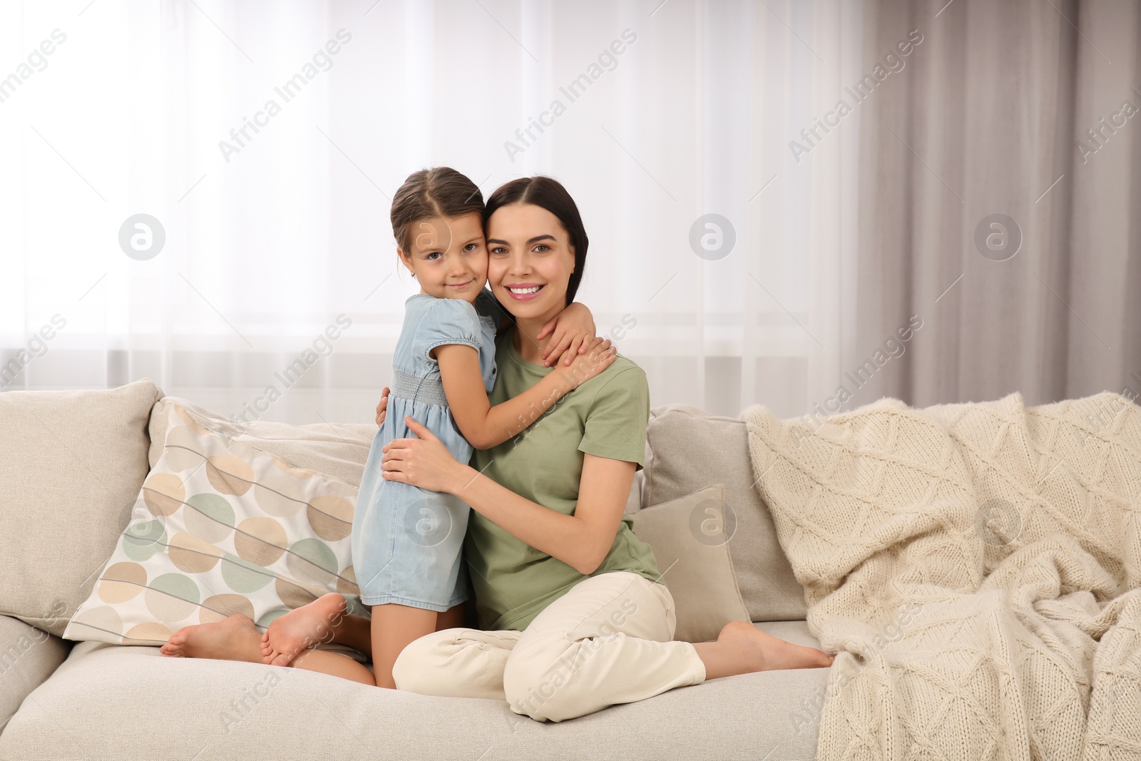 Photo of Happy woman and her cute daughter spending time together on sofa at home. Mother's day celebration