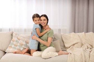 Photo of Happy woman and her cute daughter spending time together on sofa at home. Mother's day celebration