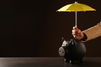 Photo of Woman holding umbrella over piggybank on dark background, closeup. Space for text