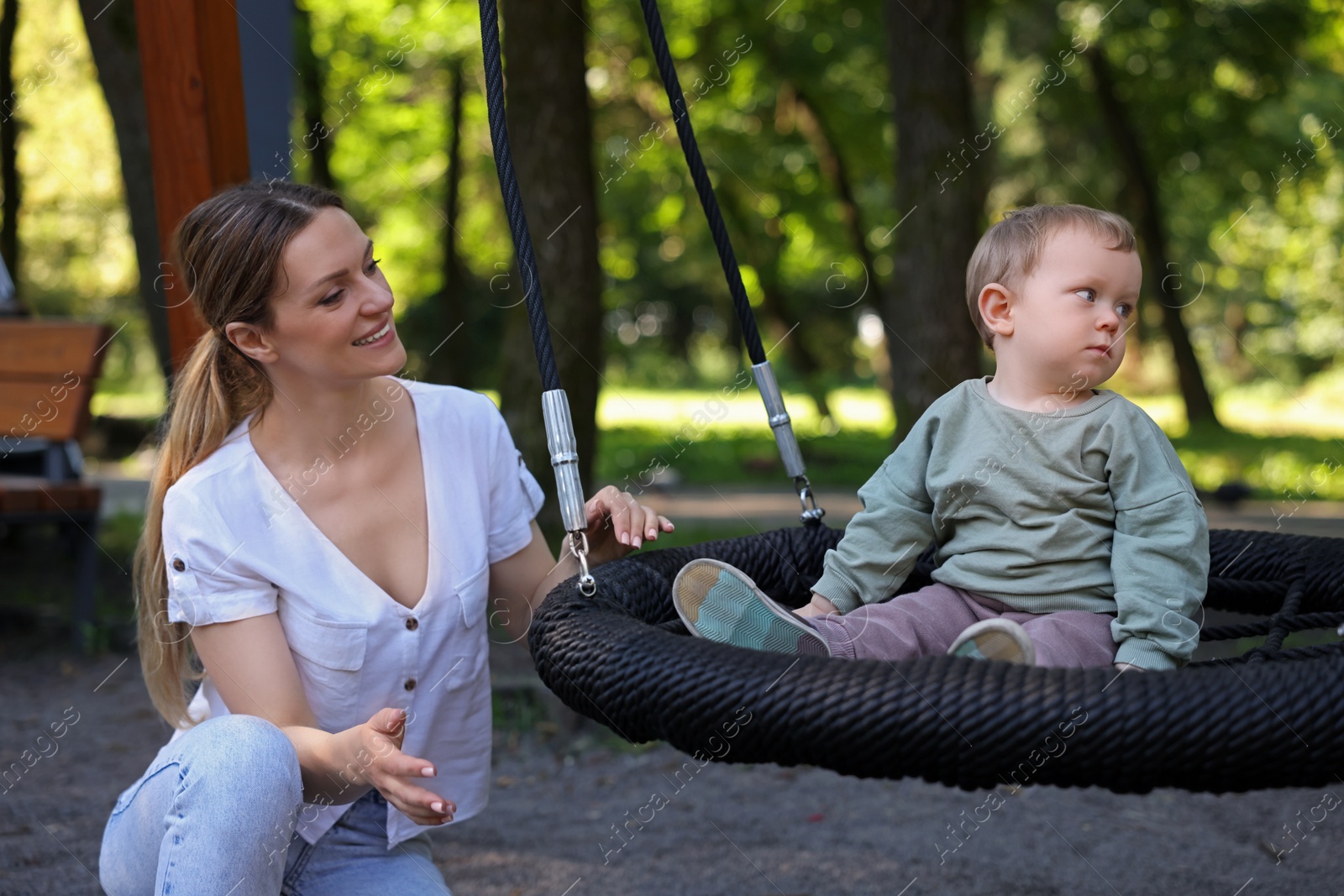 Photo of Happy nanny and cute little boy on swing outdoors