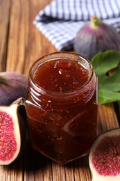 Jar of tasty sweet jam and fresh figs on wooden table, closeup