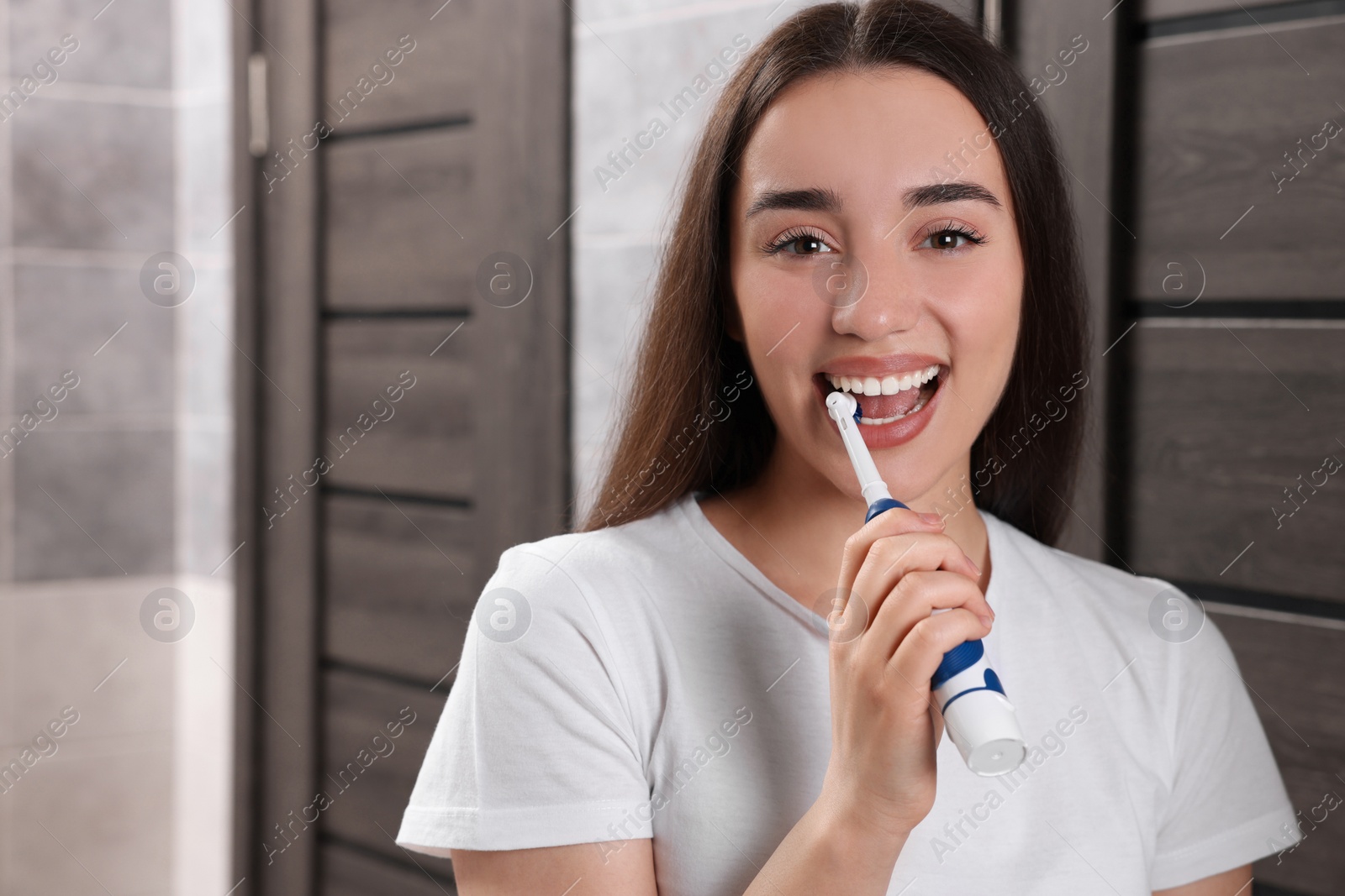 Photo of Young woman brushing her teeth with electric toothbrush in bathroom