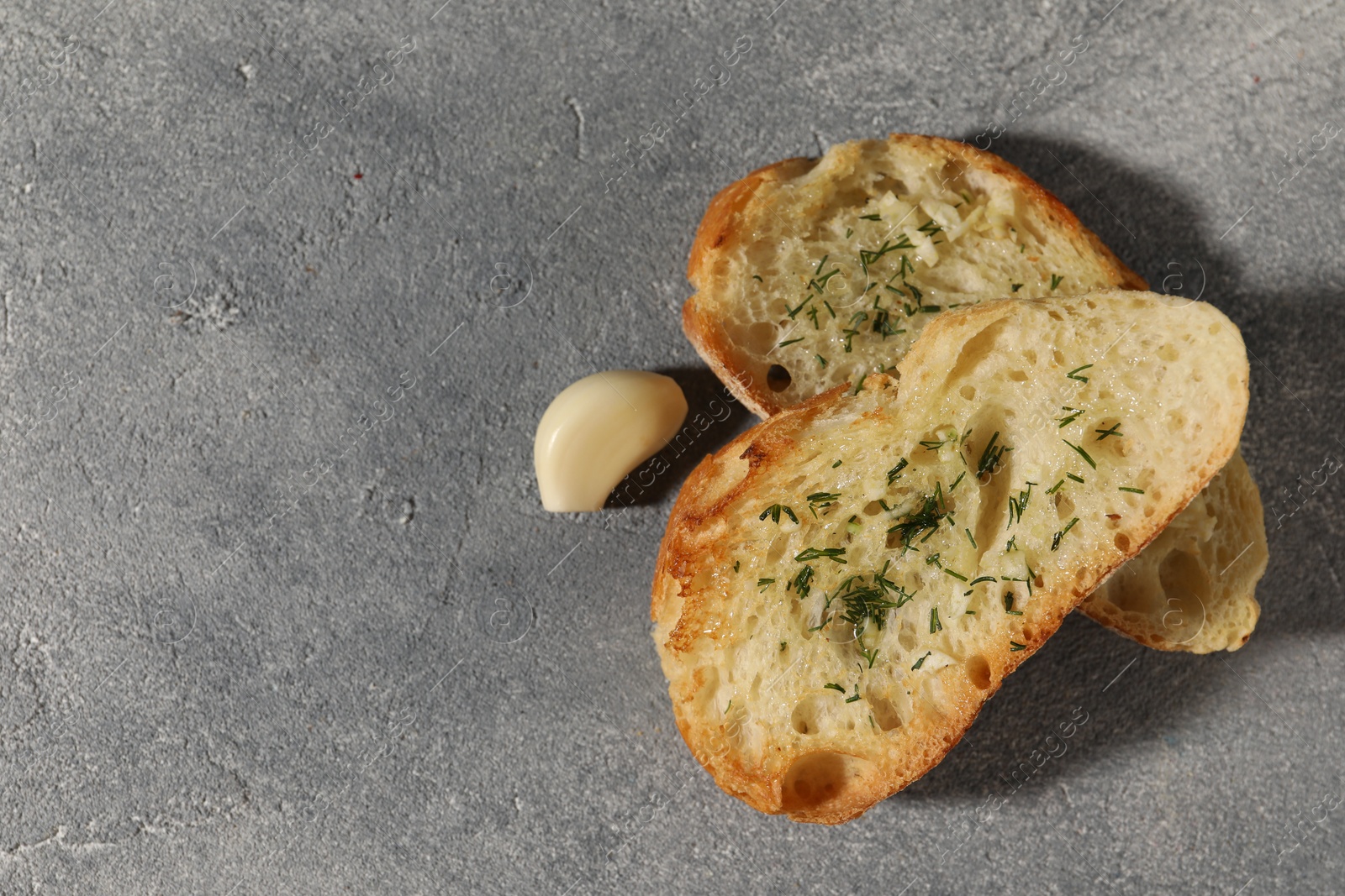 Photo of Tasty baguette with garlic and dill on grey textured table, flat lay. Space for text