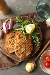 Photo of Tasty schnitzels served with onion, lemon and microgreens on grey table, flat lay