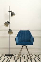 Photo of Modern blue armchair and floor lamp near white wall indoors