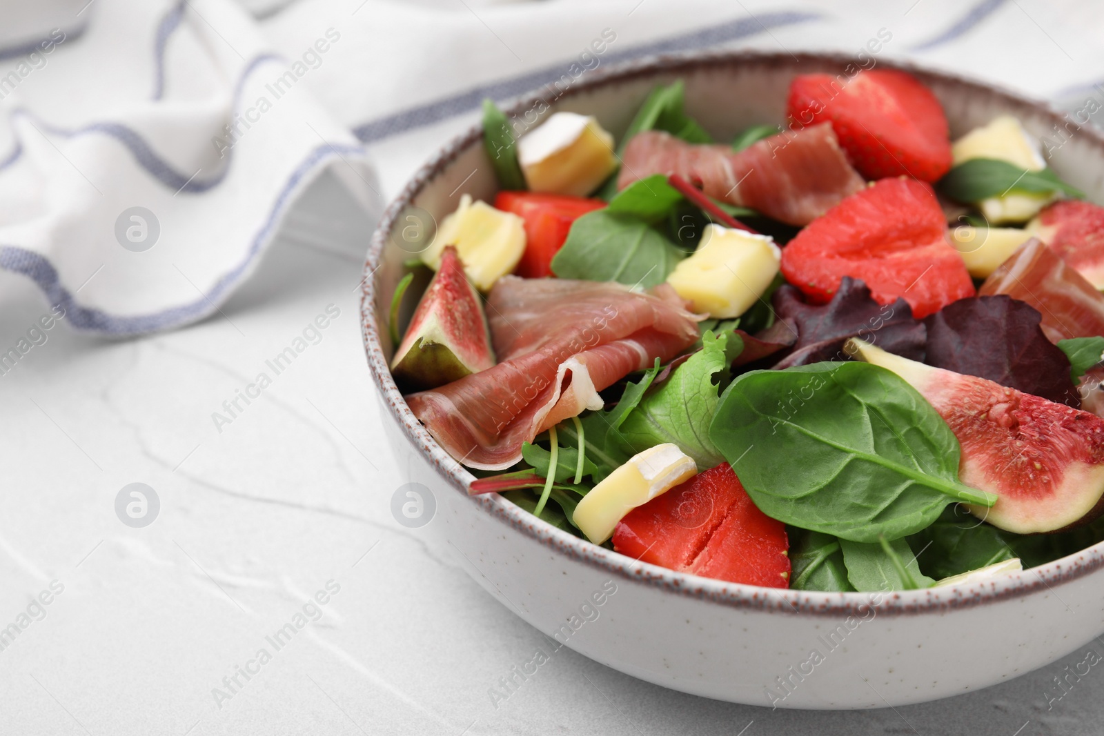 Photo of Tasty salad with brie cheese, prosciutto, strawberries and figs on white table, closeup. Space for text