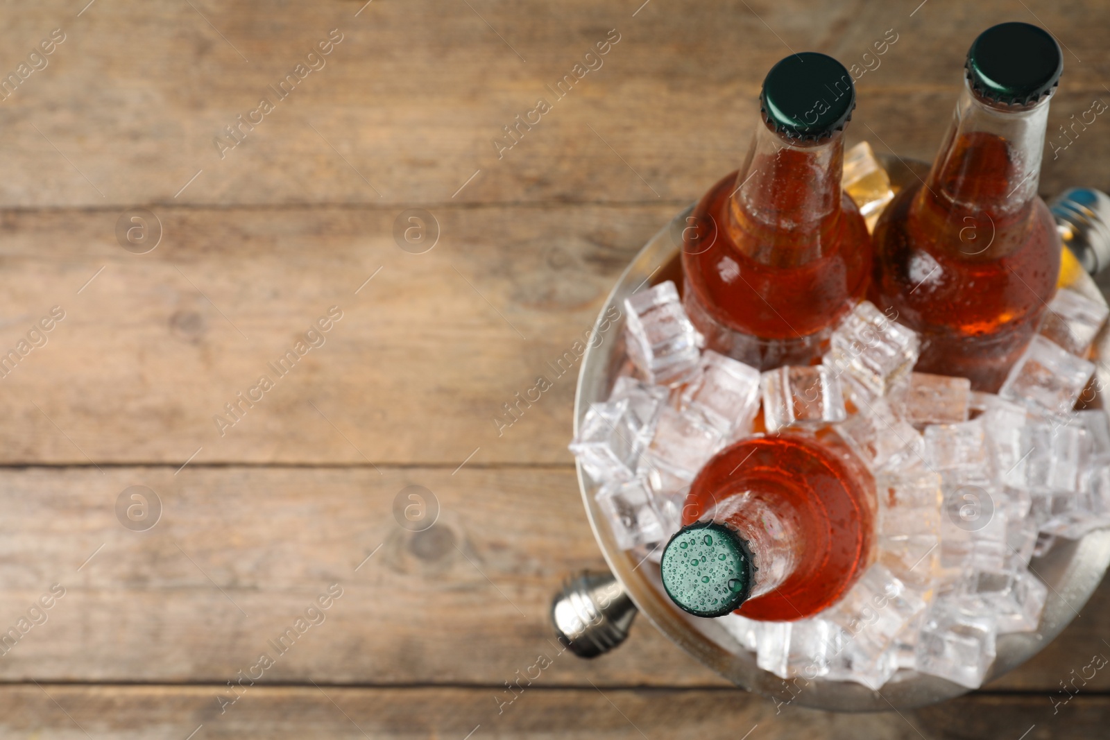 Photo of Metal bucket with beer and ice cubes on wooden background, top view. Space for text