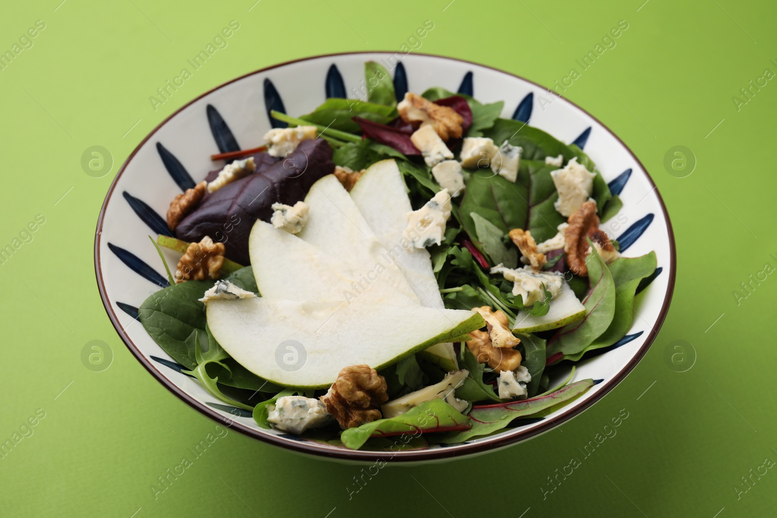Photo of Delicious pear salad in bowl on green background, closeup
