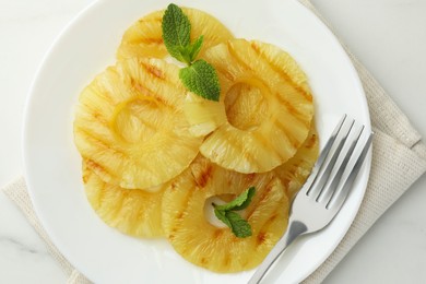 Tasty grilled pineapple slices and mint on white table, top view