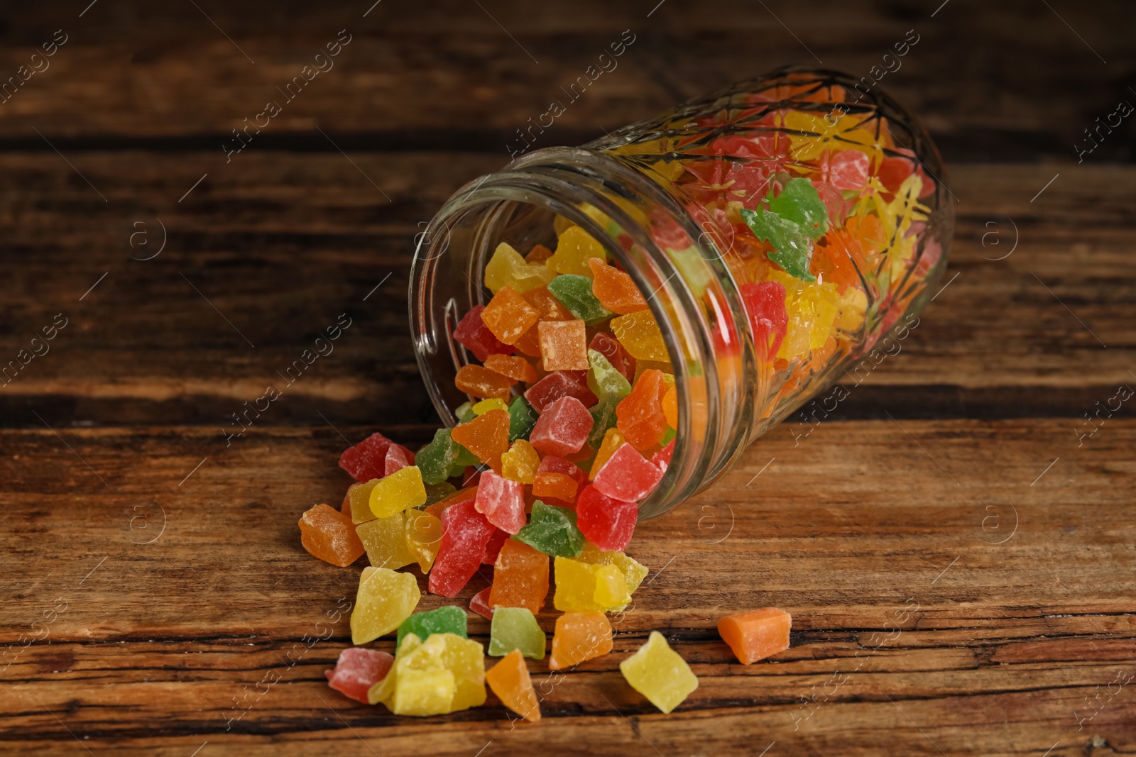 Photo of Overturned jar with mix of delicious candied fruits on wooden table