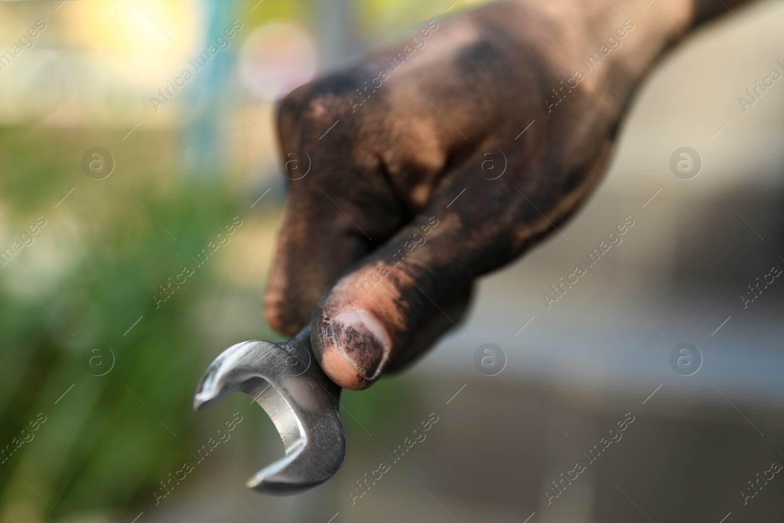 Photo of Dirty worker holding wrench on blurred background, closeup of hand