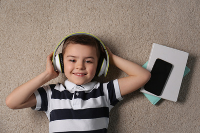 Cute little boy listening to audiobook on floor, top view
