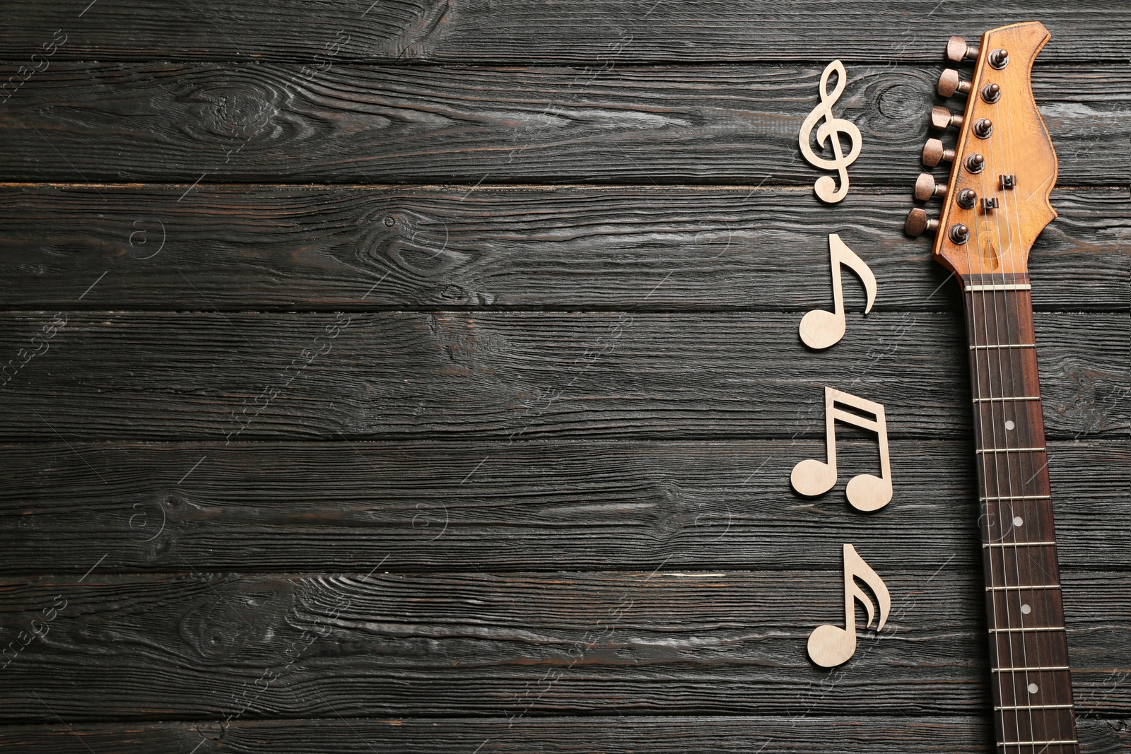 Photo of Music notes and guitar neck on wooden background, top view. Space for text
