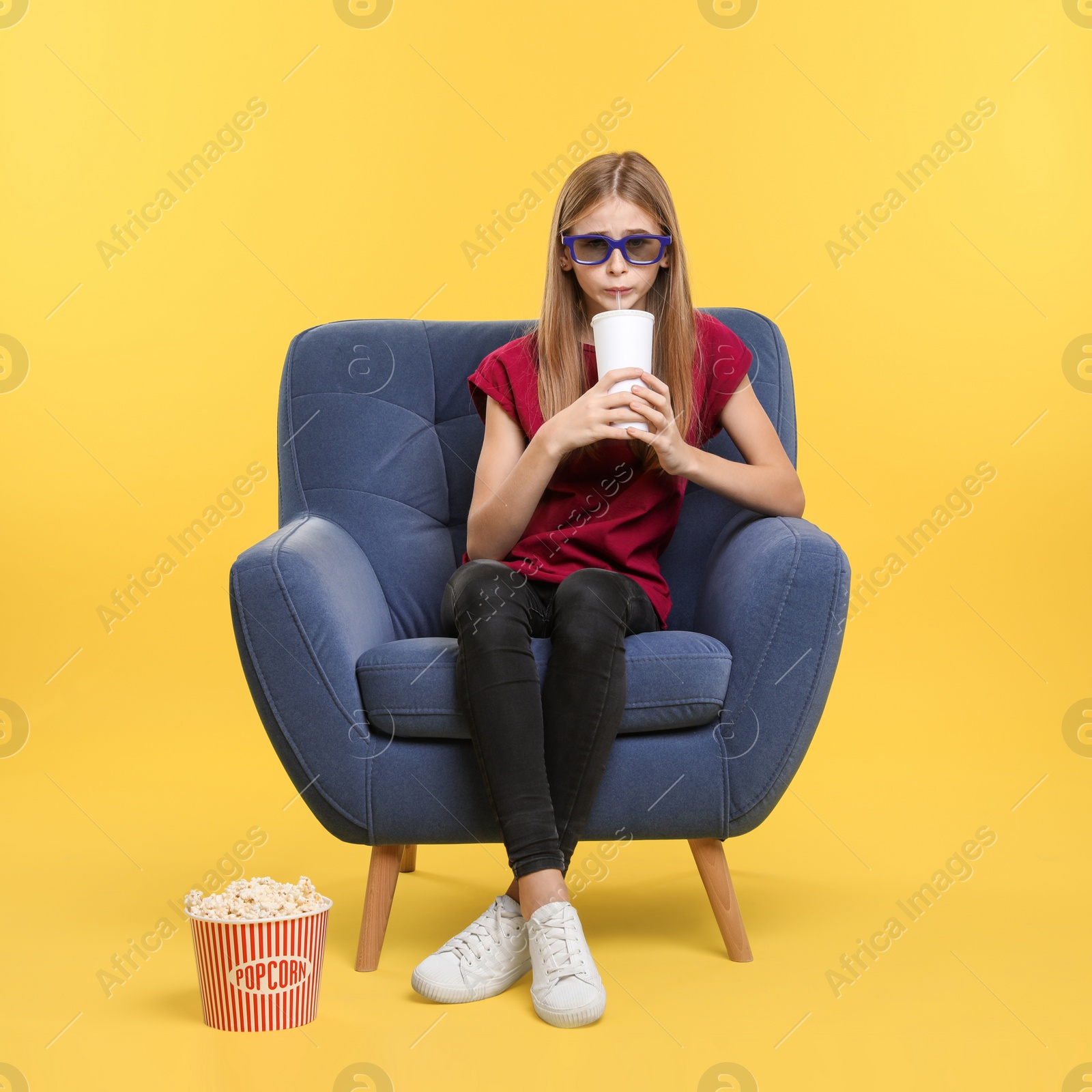 Photo of Emotional teenage girl with 3D glasses, popcorn and beverage sitting in armchair during cinema show on color background