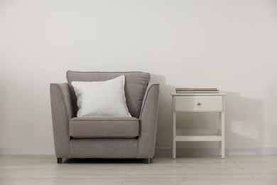 Photo of Soft white pillow on armchair and bedside table near light wall indoors