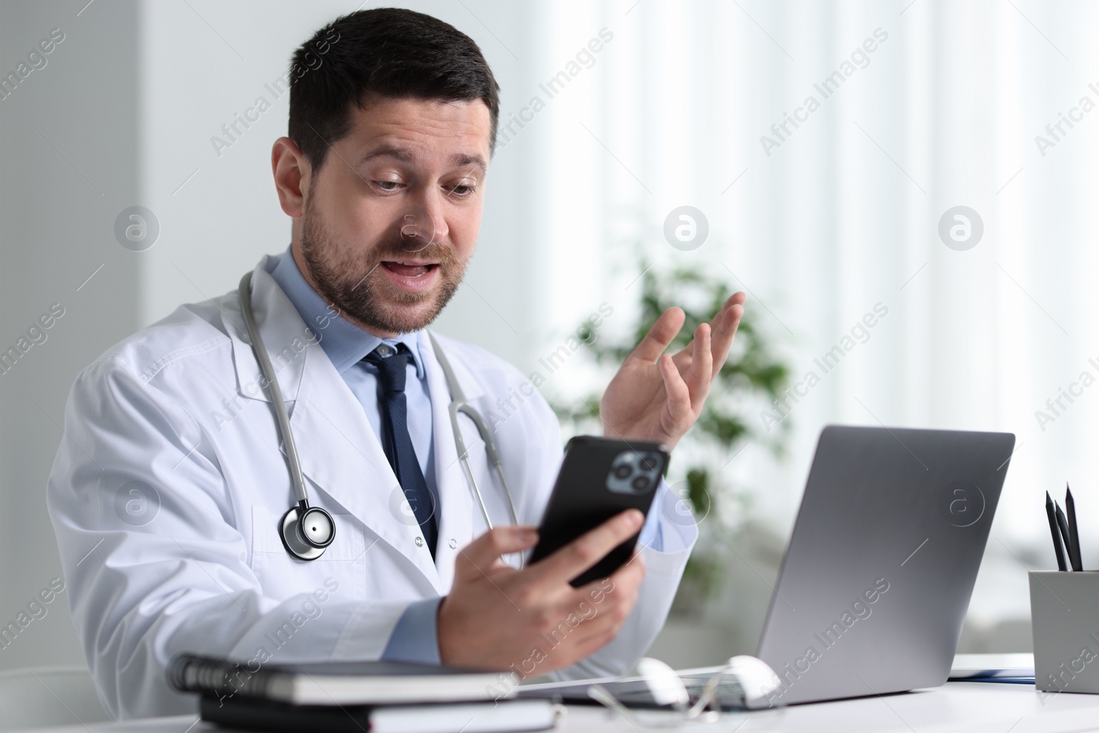 Photo of Doctor having online consultation via smartphone at table in clinic