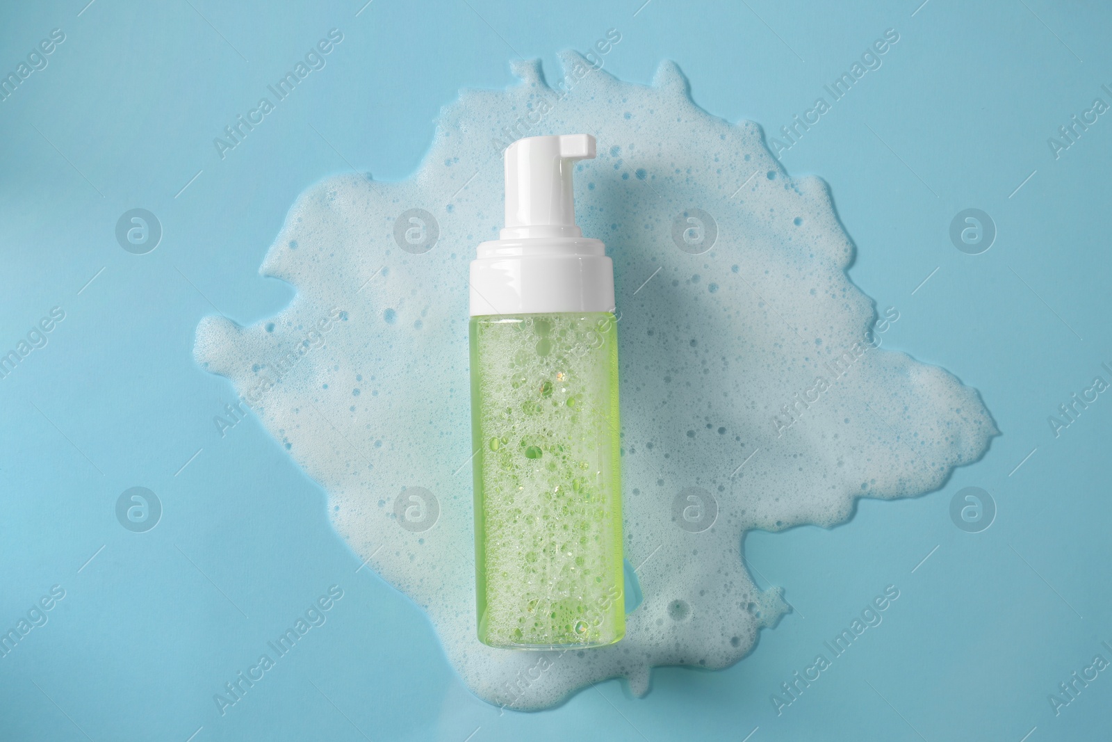 Photo of Bottle of face cleanser and white foam on light blue background, top view. Skin care cosmetic