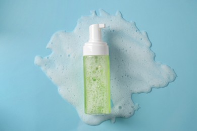 Photo of Bottle of face cleanser and white foam on light blue background, top view. Skin care cosmetic