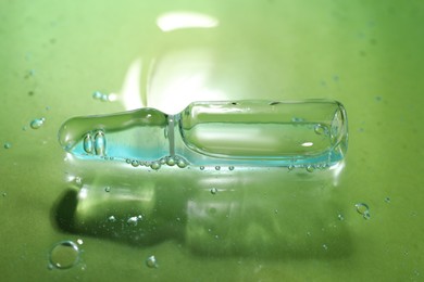 Photo of Pharmaceutical ampoule with medication in transparent gel on green background, closeup