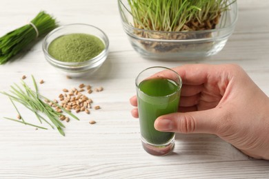 Photo of Woman holding glass of wheat grass drink at white wooden table, closeup