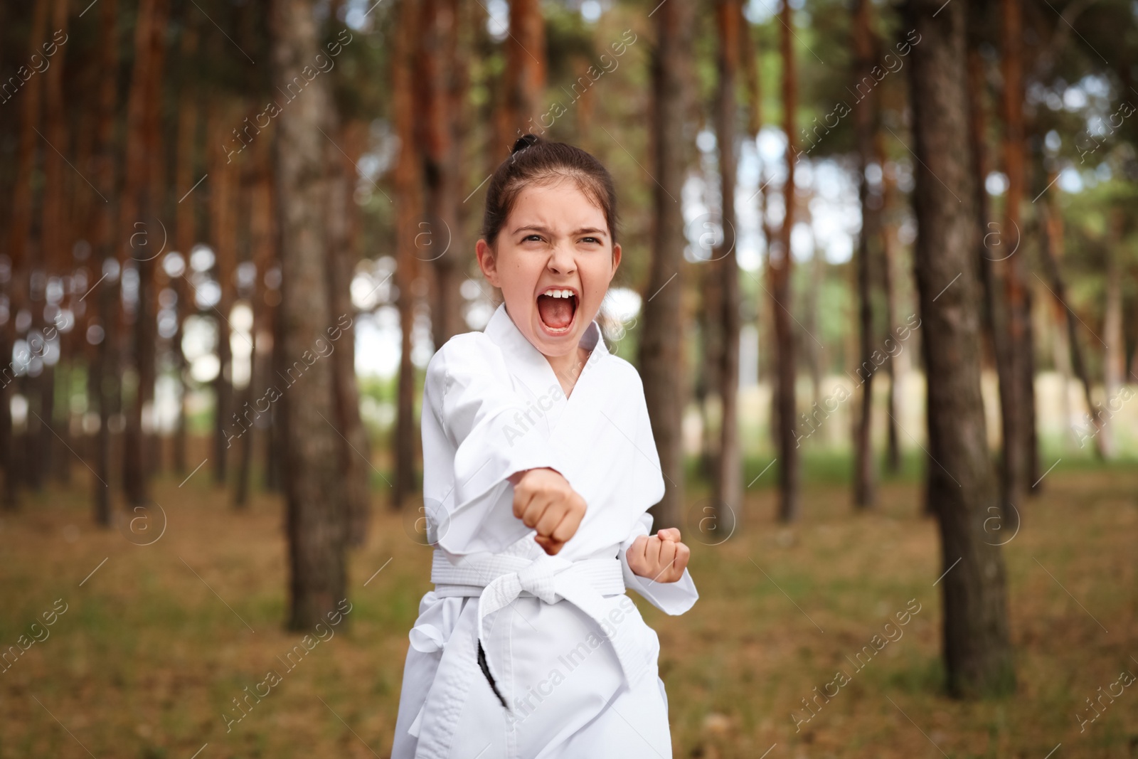 Photo of Cute little girl in kimono practicing karate in forest