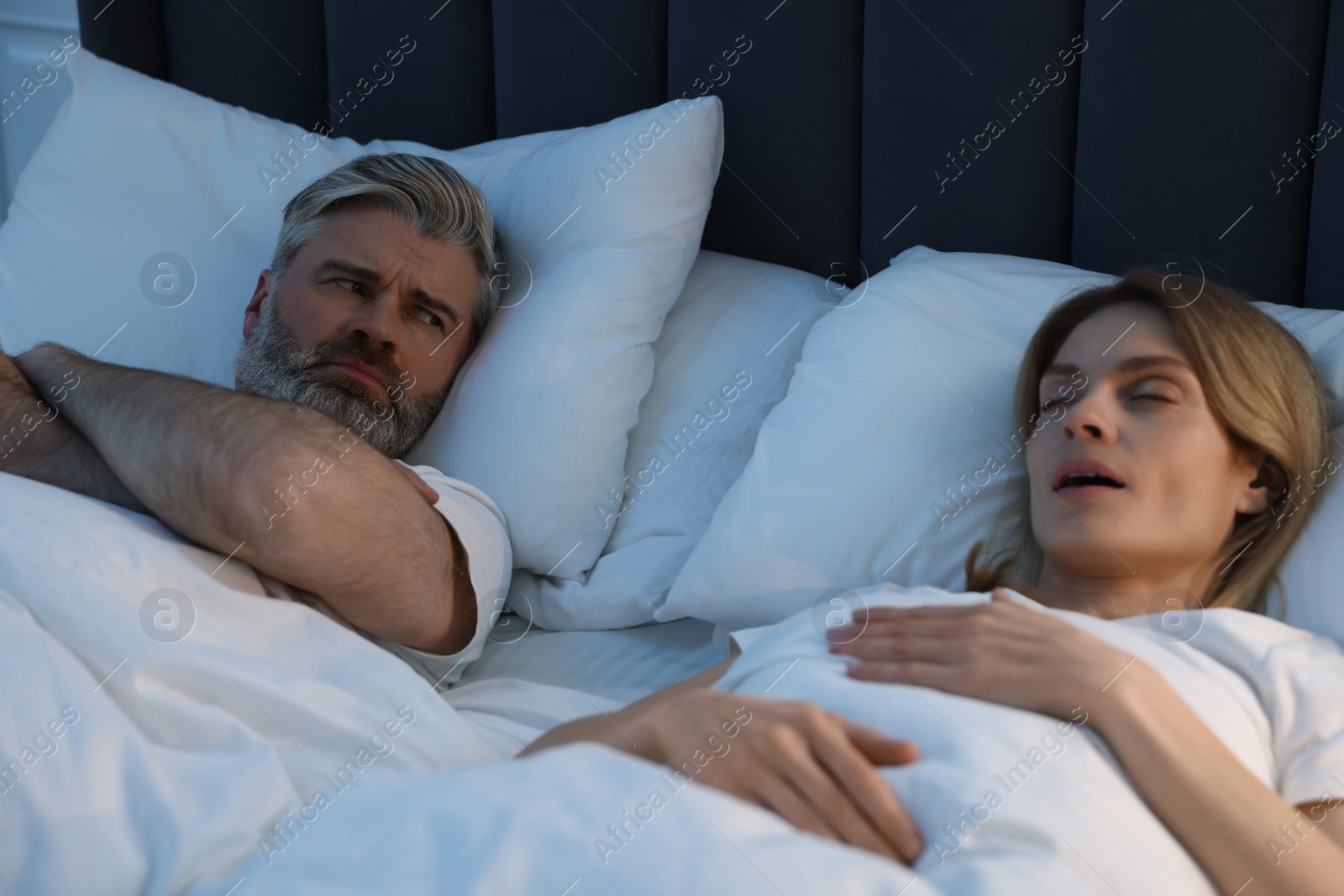 Photo of Irritated man lying near his snoring wife in bed at home