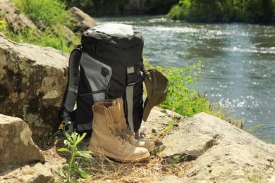 Photo of Backpack and camping equipment on stone near river. Space for text