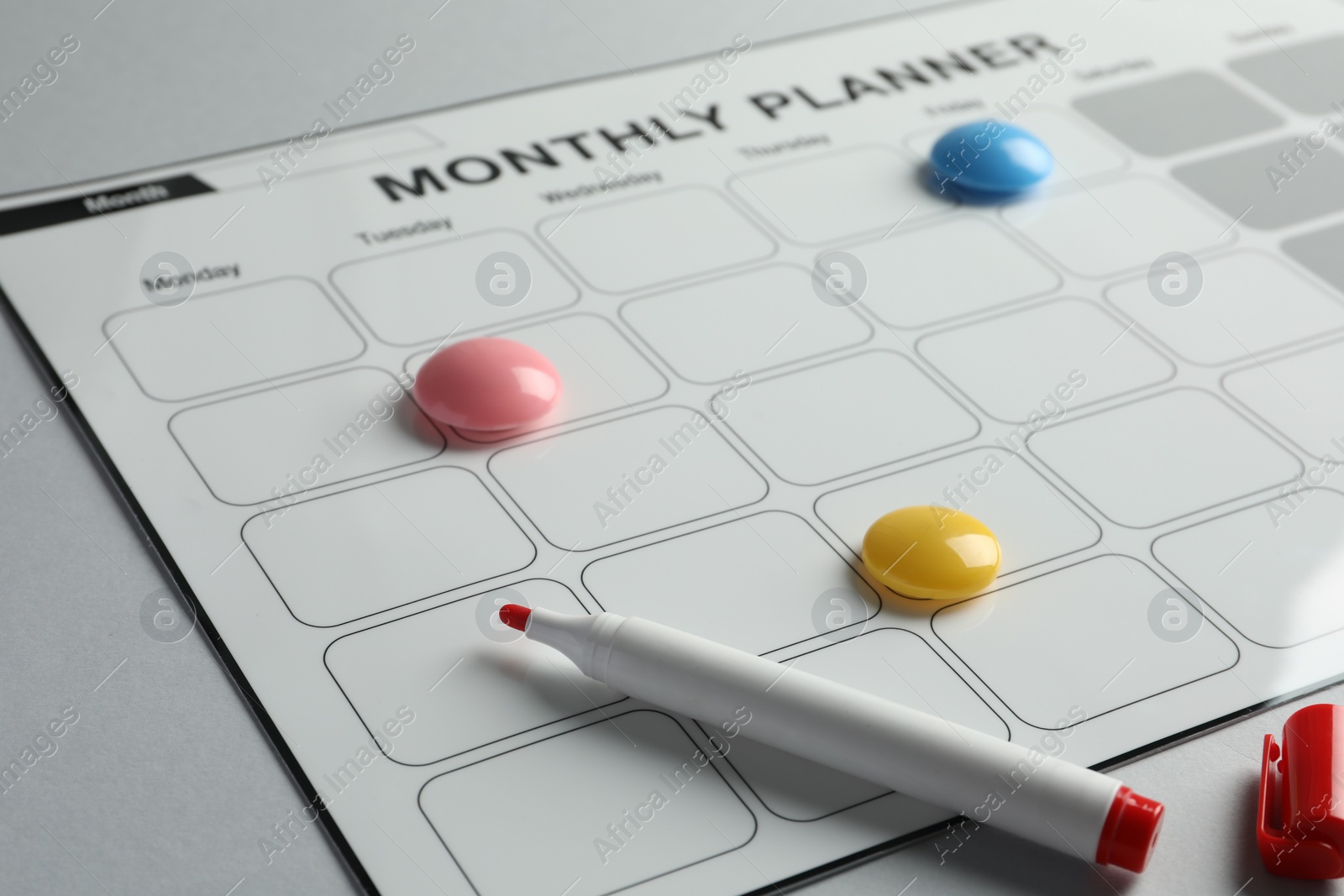 Photo of Timetable. Planner with bright magnets and red felt pen on grey table, closeup