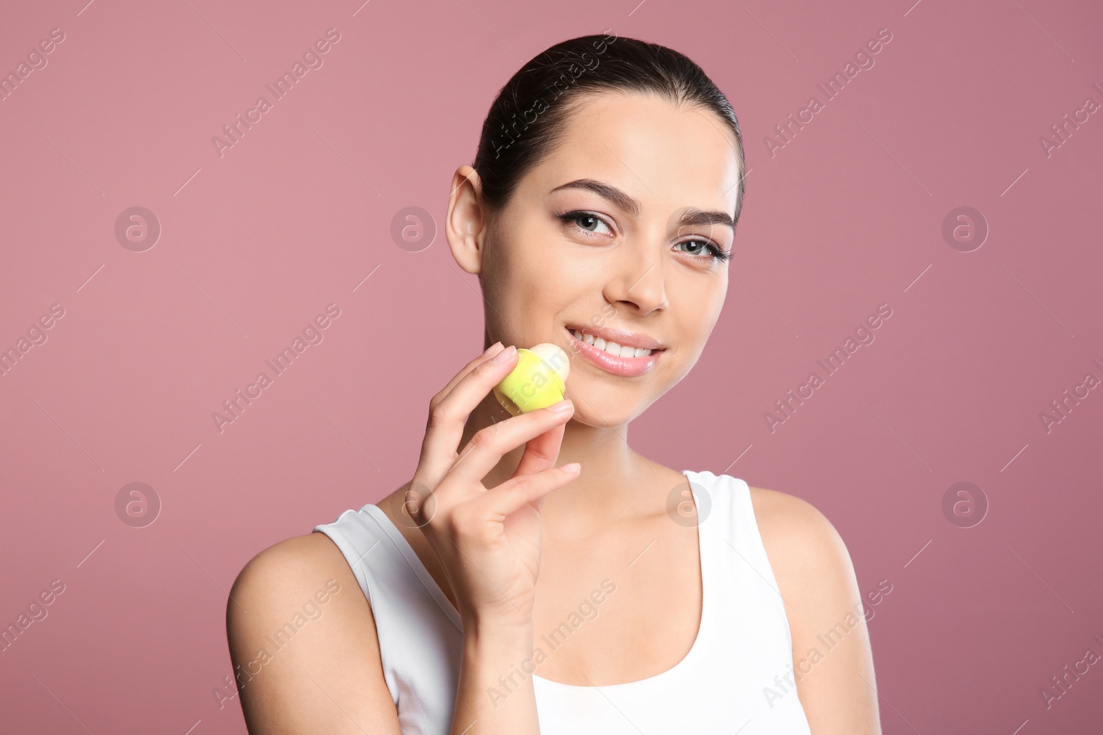 Photo of Young woman applying balm on her lips against color background