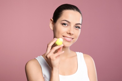 Young woman applying balm on her lips against color background