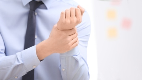 Photo of Young man suffering from wrist pain in office