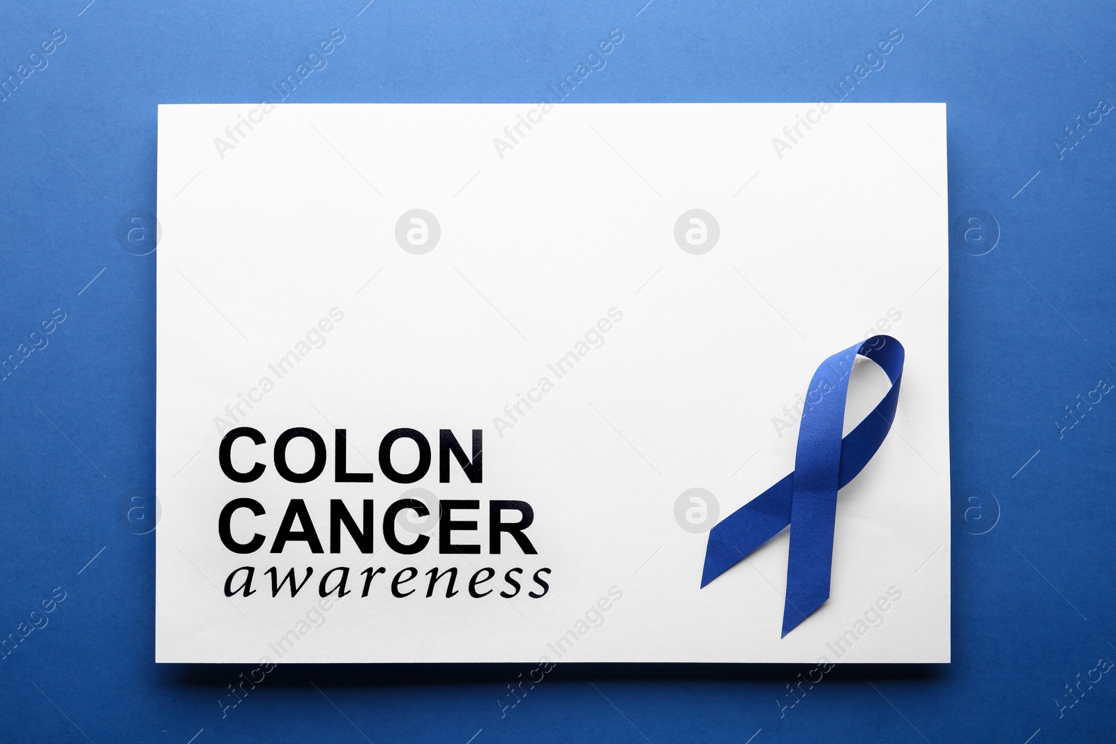 Photo of Card with words COLON CANCER AWARENESS and blue ribbon on color background, top view. Space for text