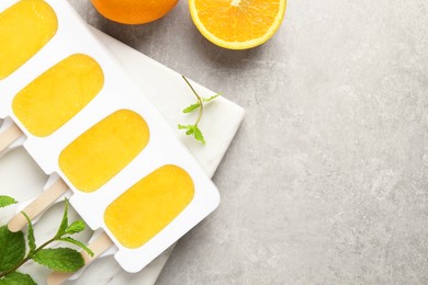 Photo of Tasty orange ice pops in mold and space for text on light grey table, flat lay. Fruit popsicle