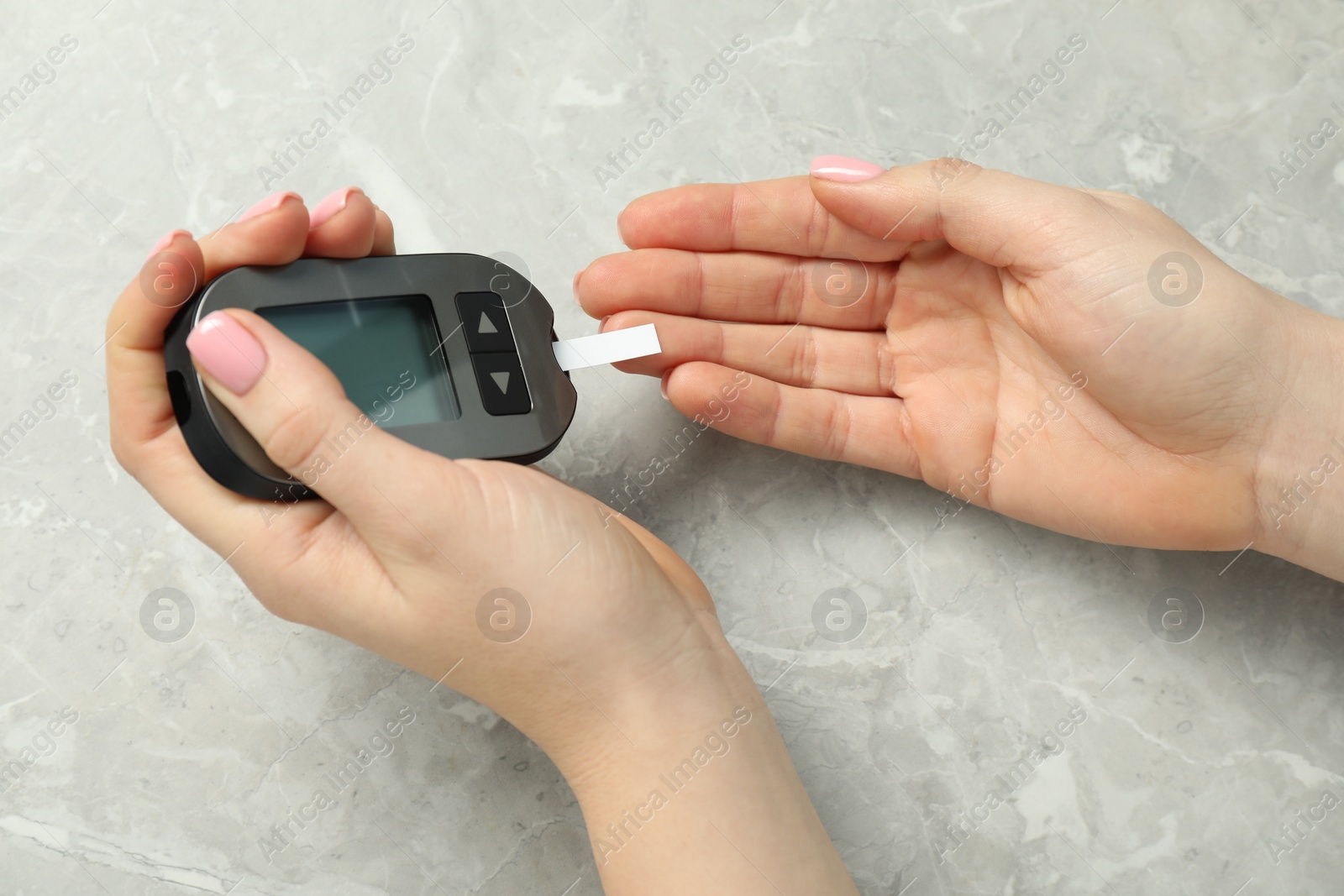 Photo of Diabetes. Woman checking blood sugar level with glucometer at gray marble table, top view