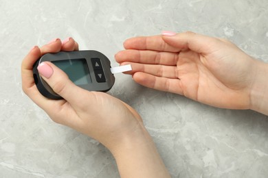 Photo of Diabetes. Woman checking blood sugar level with glucometer at gray marble table, top view