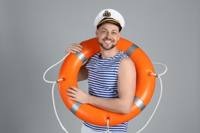 Photo of Happy sailor with orange ring buoy on grey background