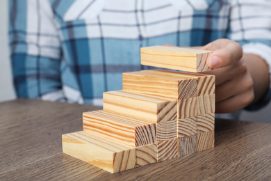 Photo of Woman building steps with wooden blocks at table, closeup. Career ladder