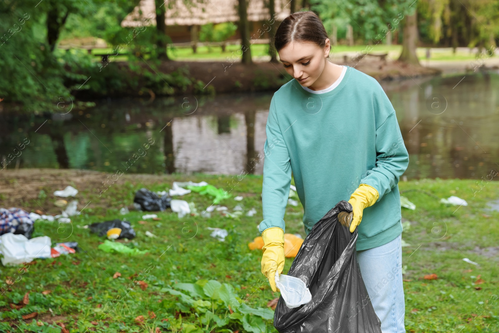 Photo of Young woman with plastic bag collecting garbage in park