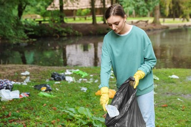 Photo of Young woman with plastic bag collecting garbage in park