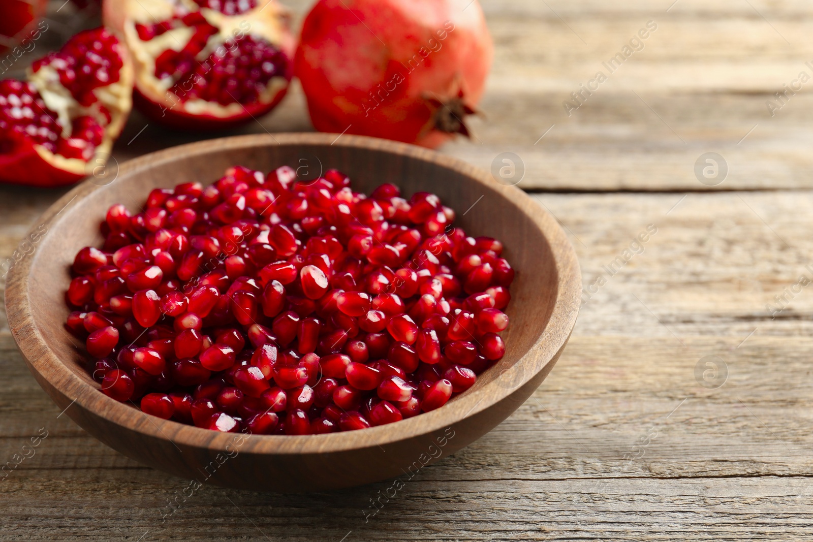 Photo of Ripe juicy pomegranate grains in bowl on wooden table. Space for text