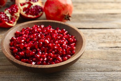 Photo of Ripe juicy pomegranate grains in bowl on wooden table. Space for text