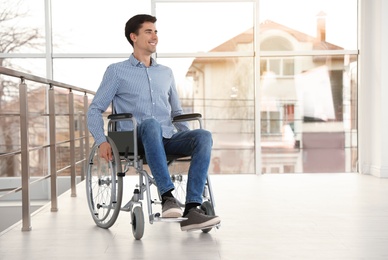 Photo of Young man in wheelchair near window indoors. Space for text