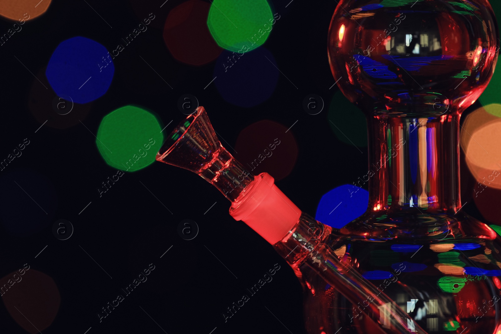 Photo of Closeup view of glass bong against blurred lights. Smoking device