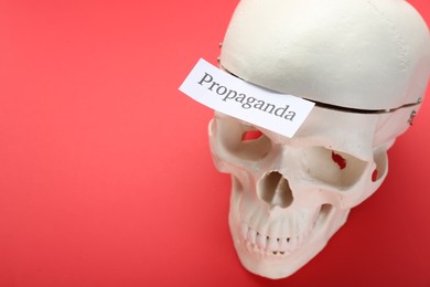 Photo of Information warfare concept. Human skull and paper card with word Propaganda on red background, above view. Space for text