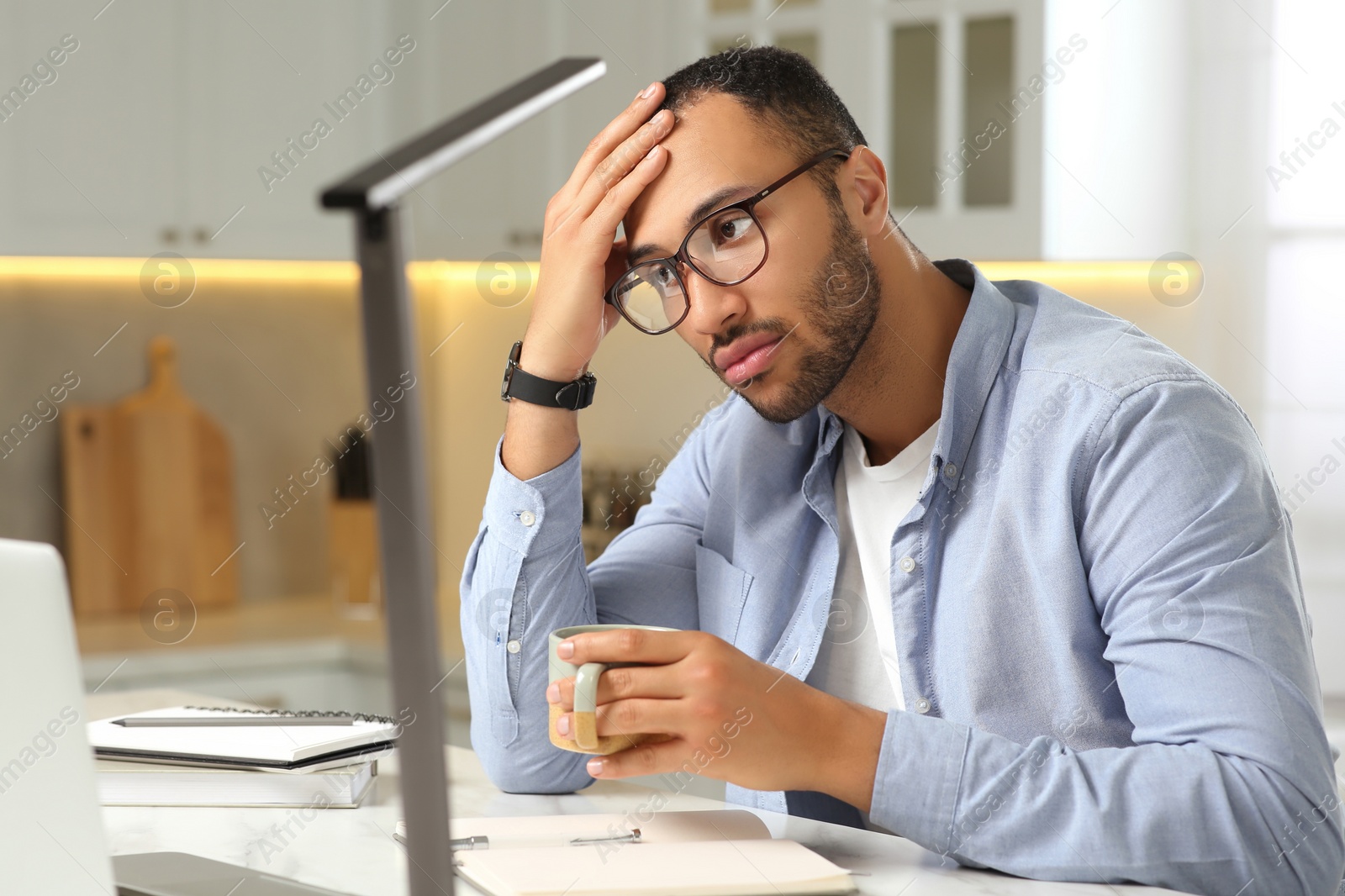 Photo of Young man working on laptop at desk in kitchen. Home office